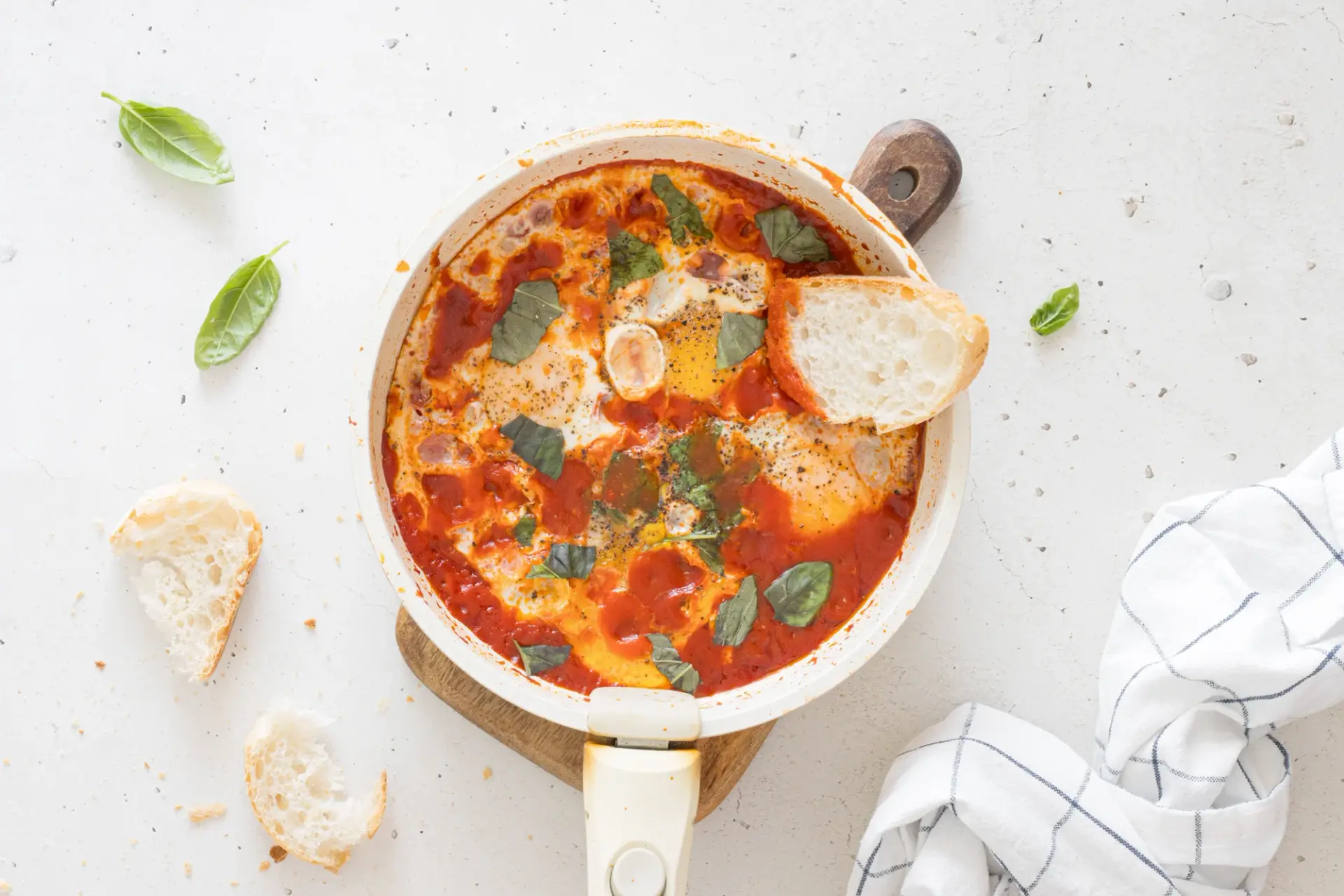 Eggs poached in tomato sauce with basil, in a pan with torn bread alongside